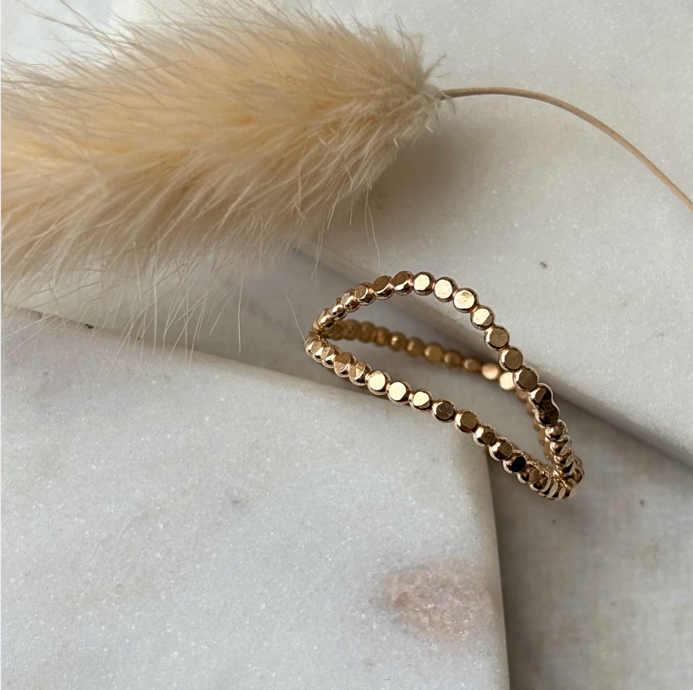 Gold ring on a light stone surface with a dried plant