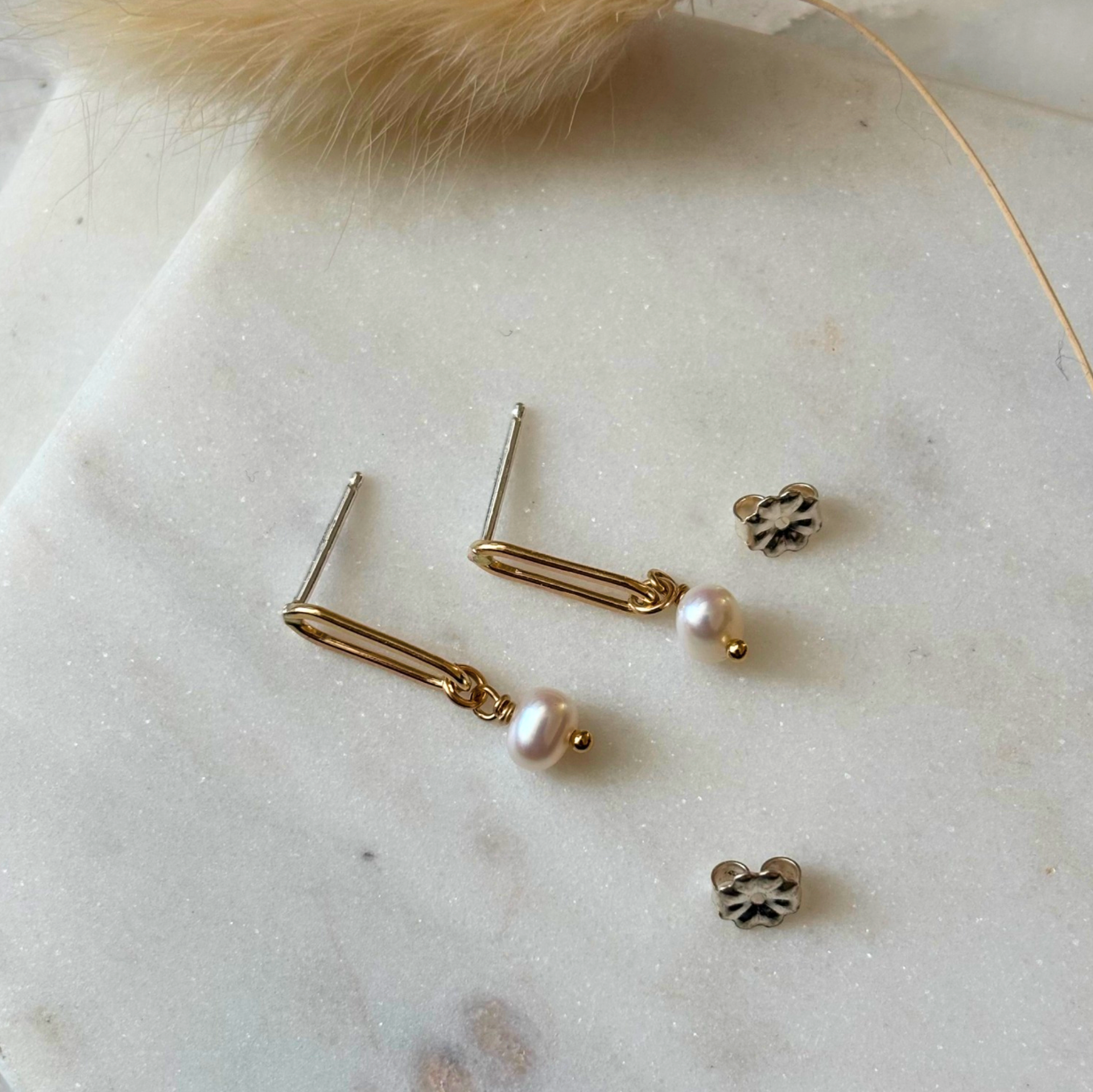 Gold and pearl earrings on a marble surface