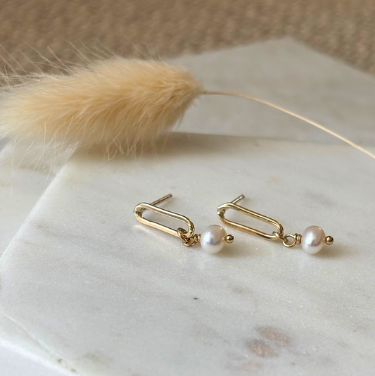 Gold earrings with pearls on a marble surface with a feather