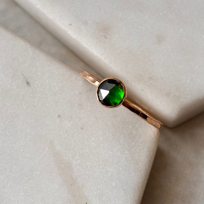 A rose-cut lab-grown emerald ring set in a 14k gold-fill band, displayed on a white marble surface.
