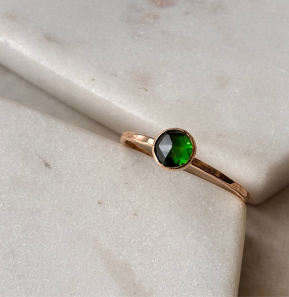A 14k gold-fill ring with a rose-cut lab-grown emerald centerpiece, displayed on a marble surface.