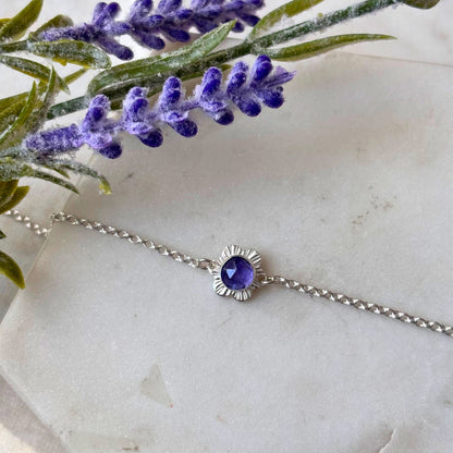 silver flower bracelet with purple stone on a marble background