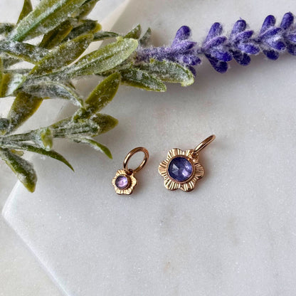 A small and larger flower charm on a marble background with tanzanite gemstone