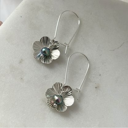 Silver flower-shaped earrings with a central pearl on a light gray surface