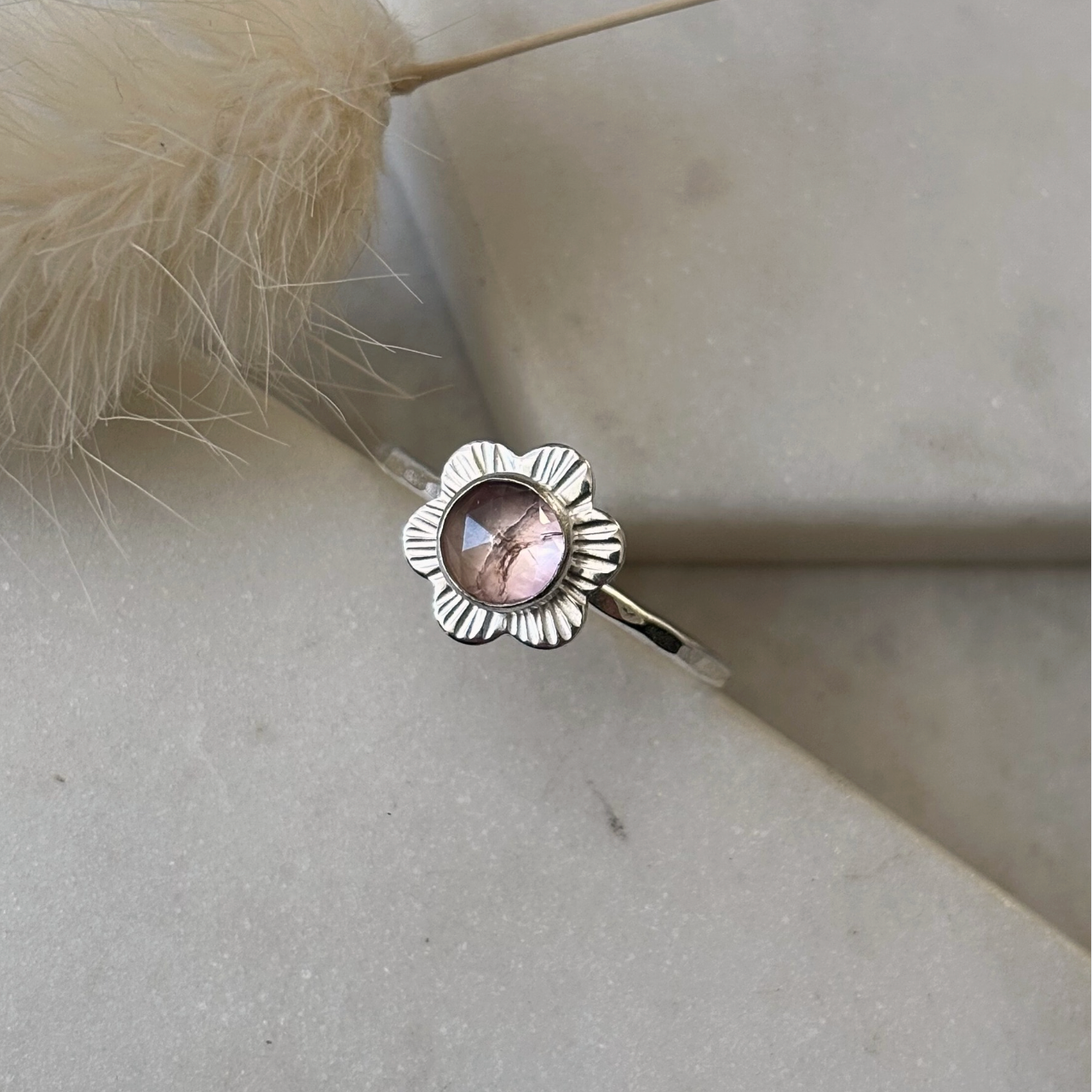 Silver flower ring with a pink gemstone on a light stone surface