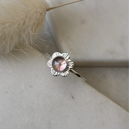 Silver flower ring with a pink gemstone on a light stone surface