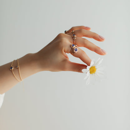 A woman holding a flower between her fingers wearing gold flower jewellery.