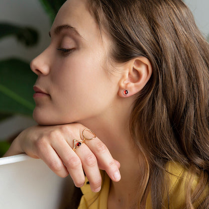 A person wearing a pair of garnet stud earrings set in silver.