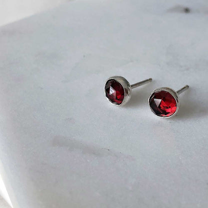 A pair of garnet stud earrings set in silver, placed on a marble surface.