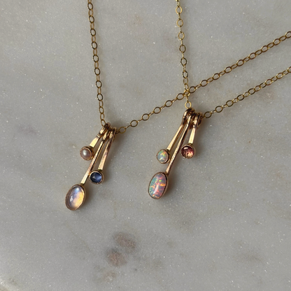 gemstone drop necklaces in gold on a marble background with blue and pink stones