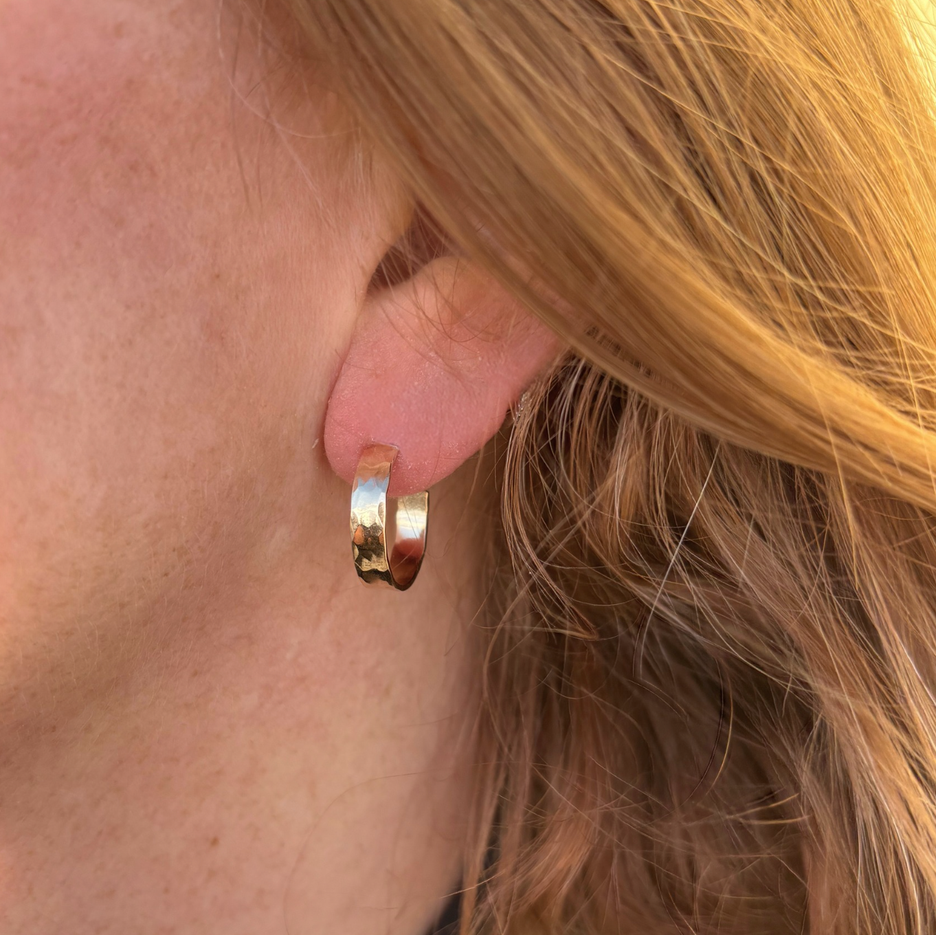Gold hoop earring worn by a person with blonde hair.