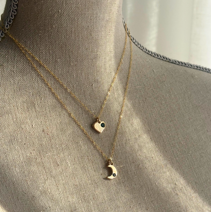 Gold necklaces with heart and moon pendants on a textured surface