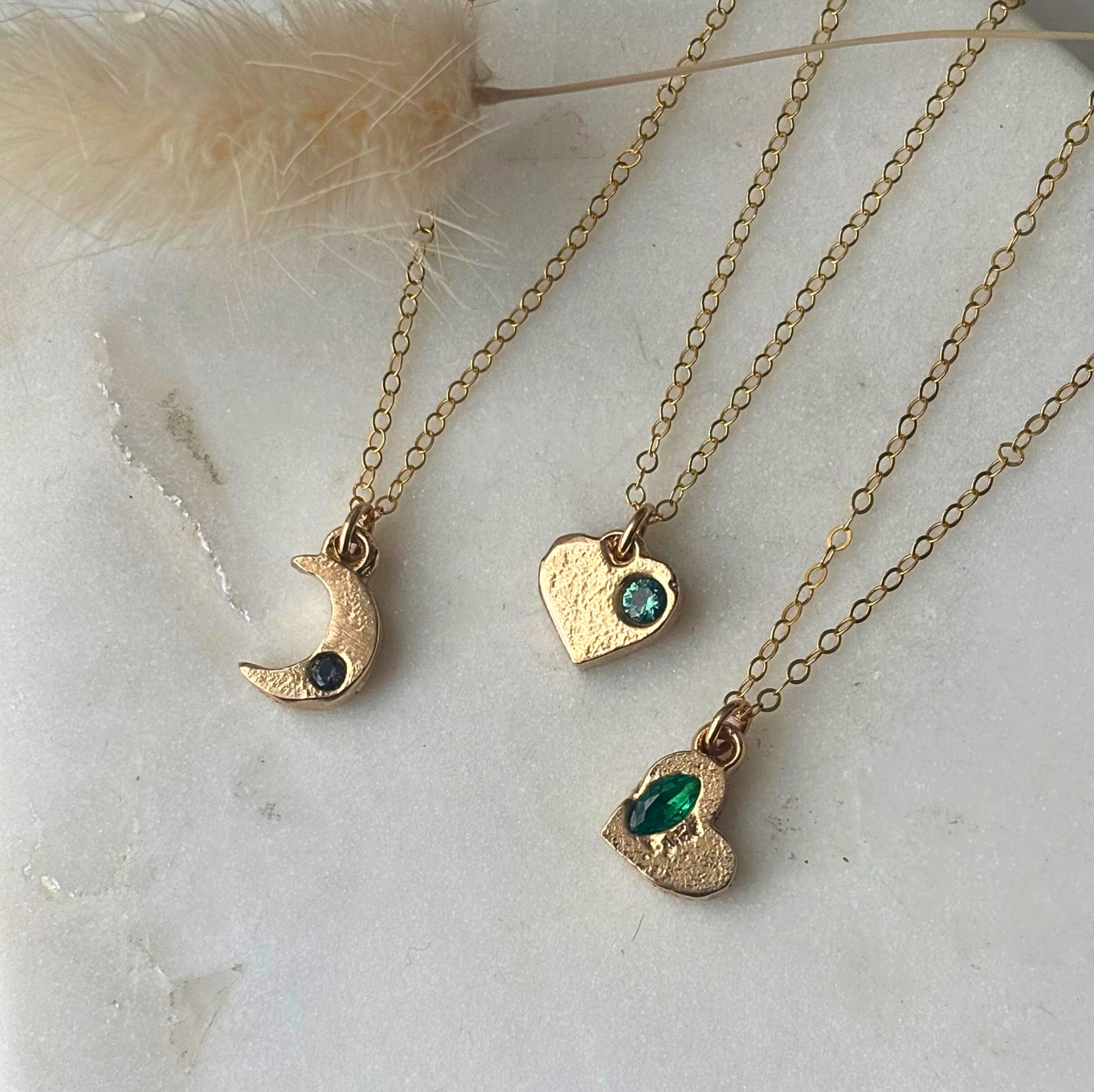 Three gold necklaces with heart and moon pendants on a light background