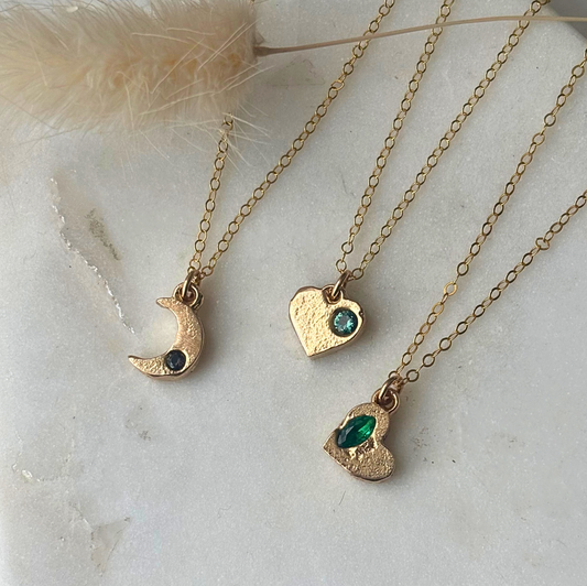 Three gold necklaces with heart and moon pendants on a light background