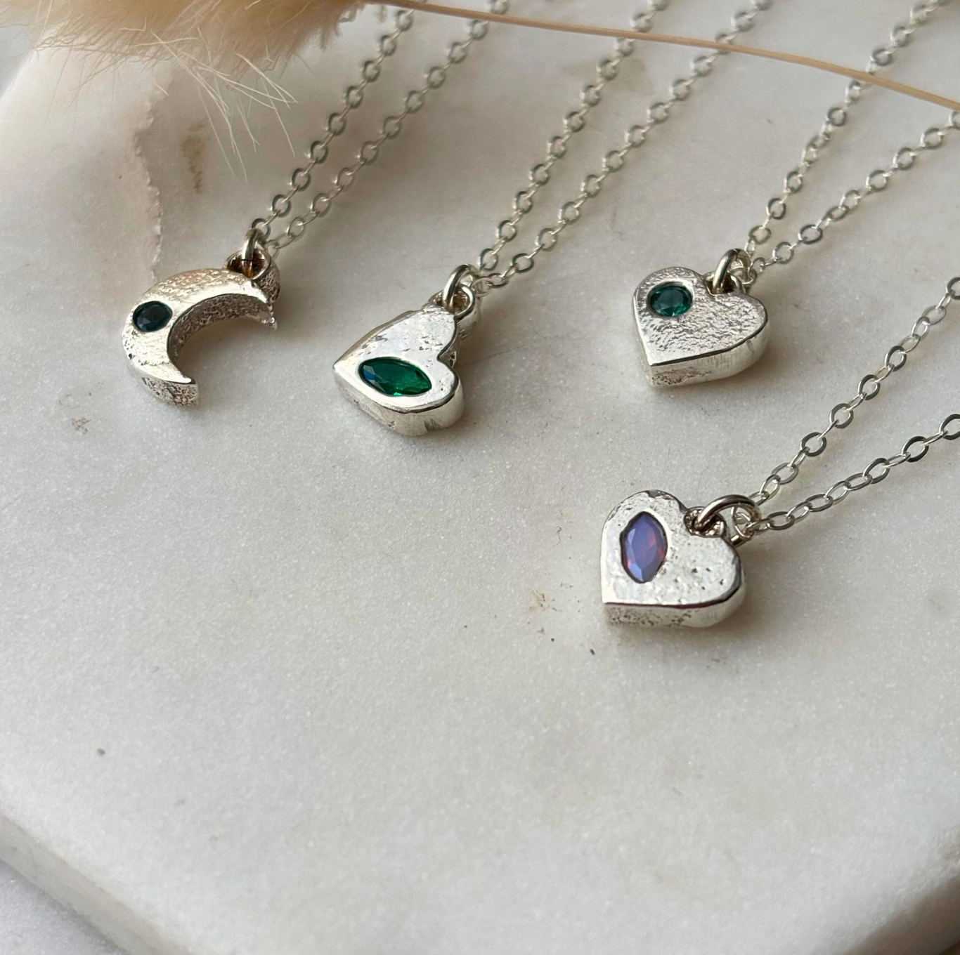 Silver necklaces with heart and crescent moon pendants on a white surface