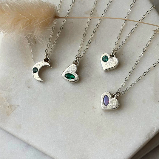 Four silver necklaces with heart and crescent moon pendants on a marble surface.