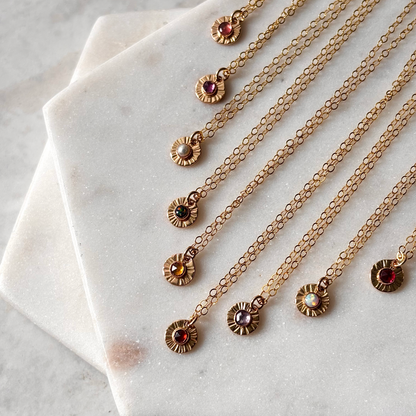 Gold necklaces with various coloured gemstone pendants on a marble surface