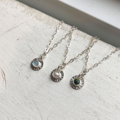 Silver necklaces with various coloured gemstone pendants on a marble 