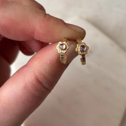 A hand holding gold hoop earrings above a textured marble surface