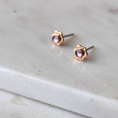 A pair of mini flower stud earrings with textured details and tanzanite gemstones, placed on a marble surface.