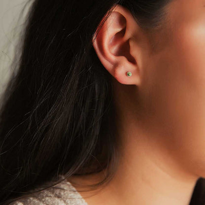 Small round stud earrings made with peridot stones, worn on an ear.