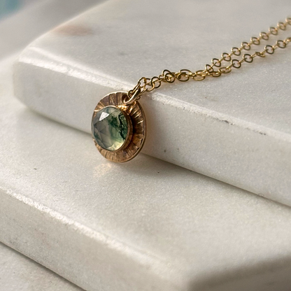 A gold moss agate pendant on a marble background.