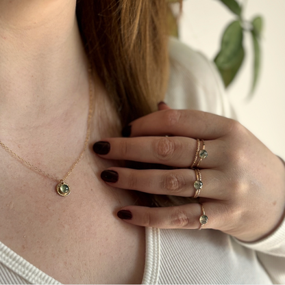 A person wearing a gold moss agate pendant and rings.