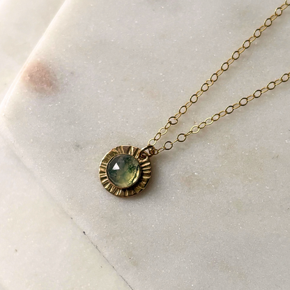 A gold-fill or sterling silver necklace with a central moss agate gemstone pendant, displayed on a marble surface.