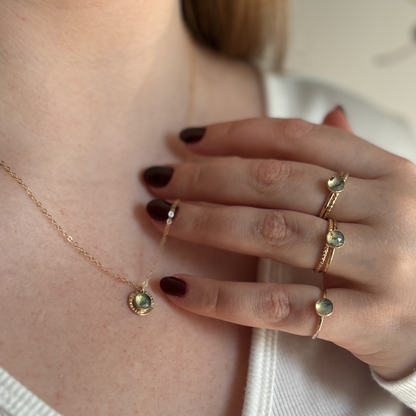 A person wearing a gold moss agate pendant and rings.