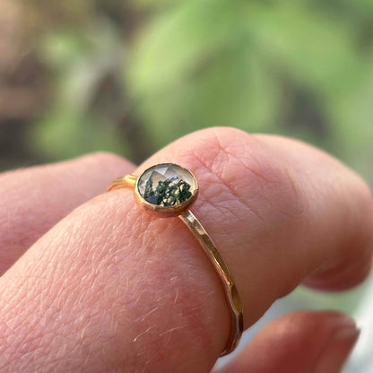 A finger wearing a gold moss agate ring.