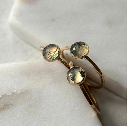 A stack of three rings, featuring moss agate stones set in gold-fill, placed on a marble surface.