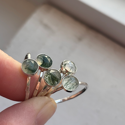 Fingers holding silver moss agate rings.