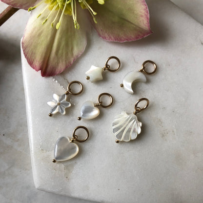 A collection of handmade Mother of Pearl charms in various shapes such as heart, star, moon, flower, and shell on a marble surface.