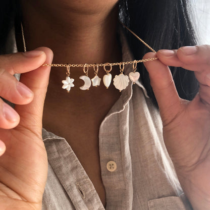 A collection of handmade Mother of Pearl charms in various shapes such as heart, star, moon, flower, and shell dangling from a chain.