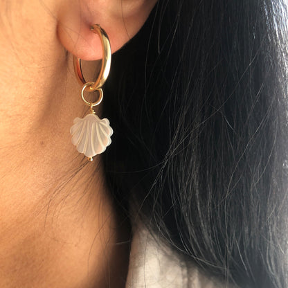 A Mother of Pearl charms dangling from a gold hoop earring.