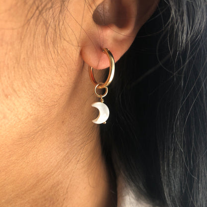 A Mother of Pearl charm moon dangling from a gold hoop earring.