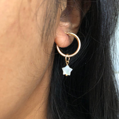 A Mother of Pearl charm star dangling from a gold hoop earring.