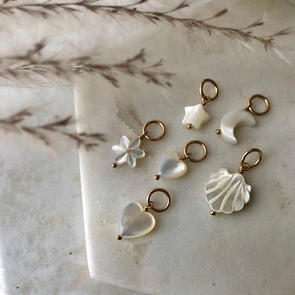 A collection of handmade Mother of Pearl charms in various shapes such as heart, star, moon, flower, and shell.