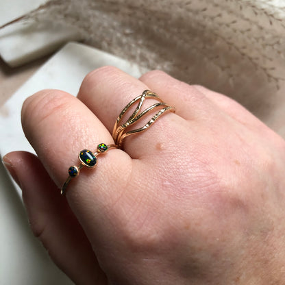 A hand wearing an oval triple gemstone ring with black opal set in gold displayed on a white surface.
