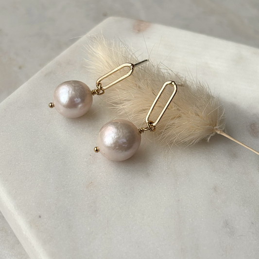 Pearl earrings with gold hooks on a marble surface with a feather.