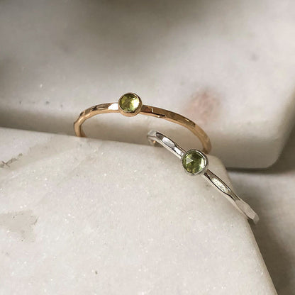 Two peridot gemstone rings in silver and gold on a marble background.