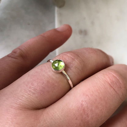 A person wearing a sterling silver ring with a peridot gemstone on their finger.
