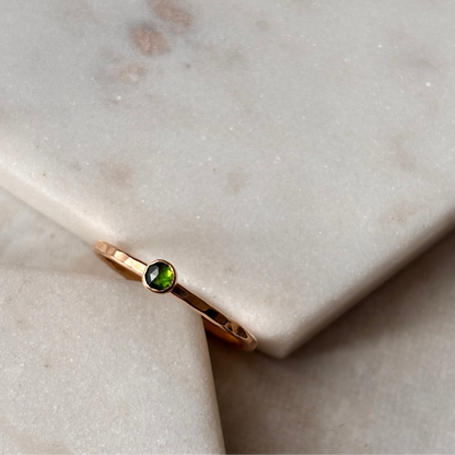 A petite emerald ring with a gold band, set on a marble surface.