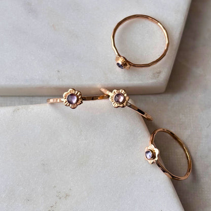A collection of delicate floral rings with a rose-cut tanzanite gemstone, crafted in 14k gold-fill, displayed on a marble surface.