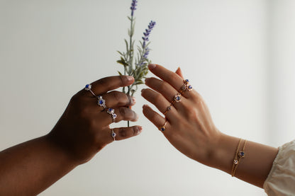 Two women's hands displaying flower rings, passing a lavender sprig between them.