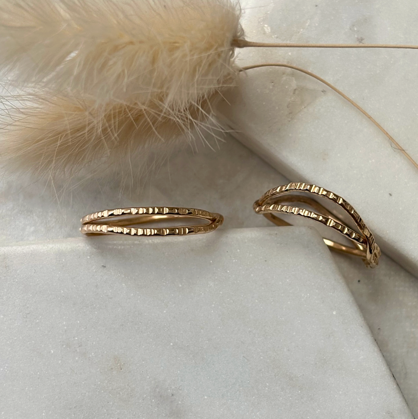 Gold rings on a light stone surface with dried grass and feathers.