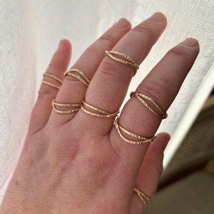 Hand wearing multiple gold rings on a neutral background