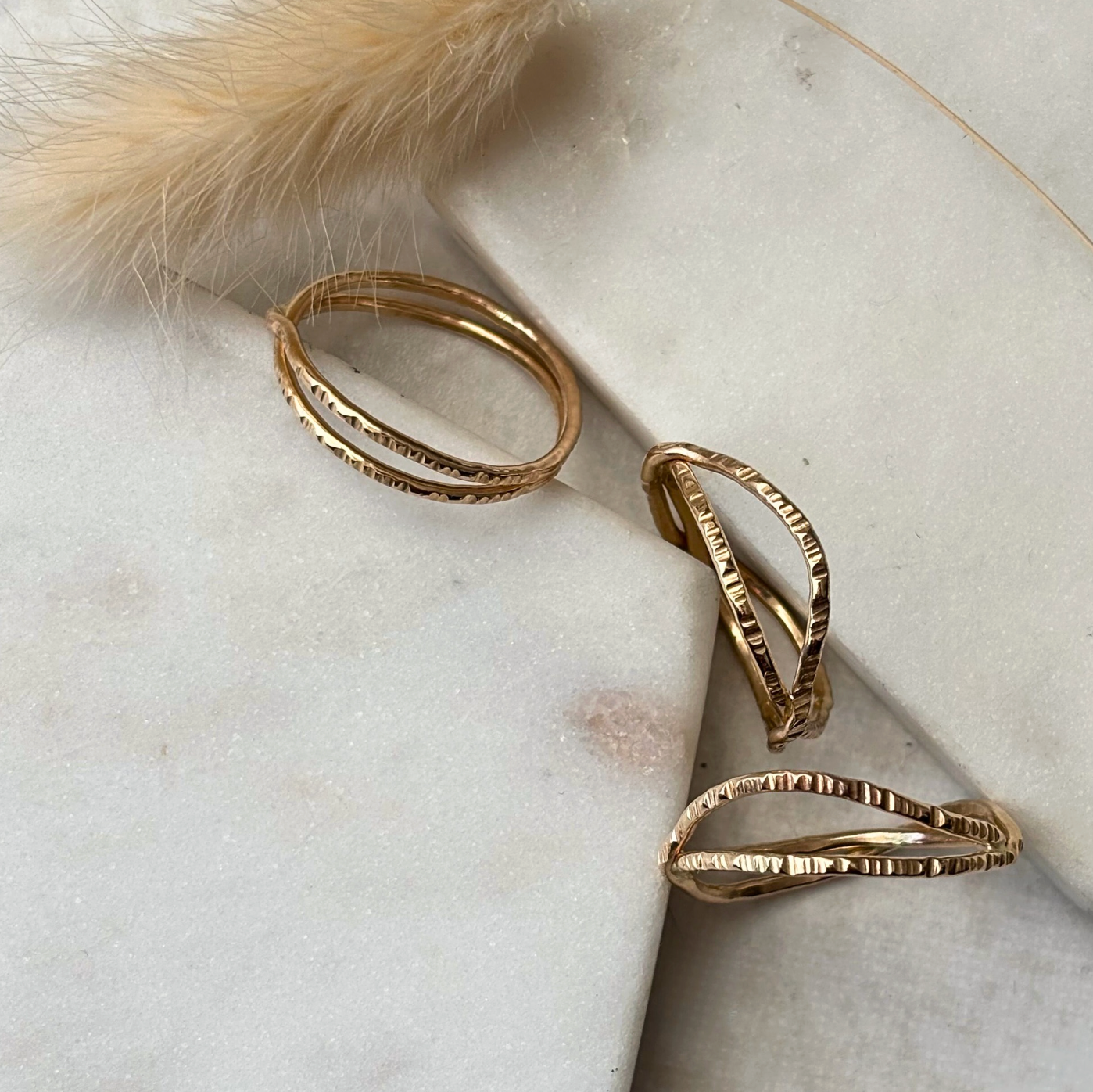 Gold textured rings on a marble surface with a fluffy object in the corner.