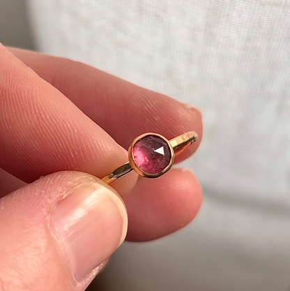 Gold ring with a pink gemstone held between fingers against a neutral background