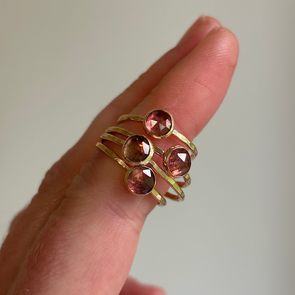 Gold ring with pink gemstones on a finger against a neutral background
